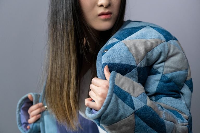 A fashionable woman poses in a denim jacket against a gray studio background.