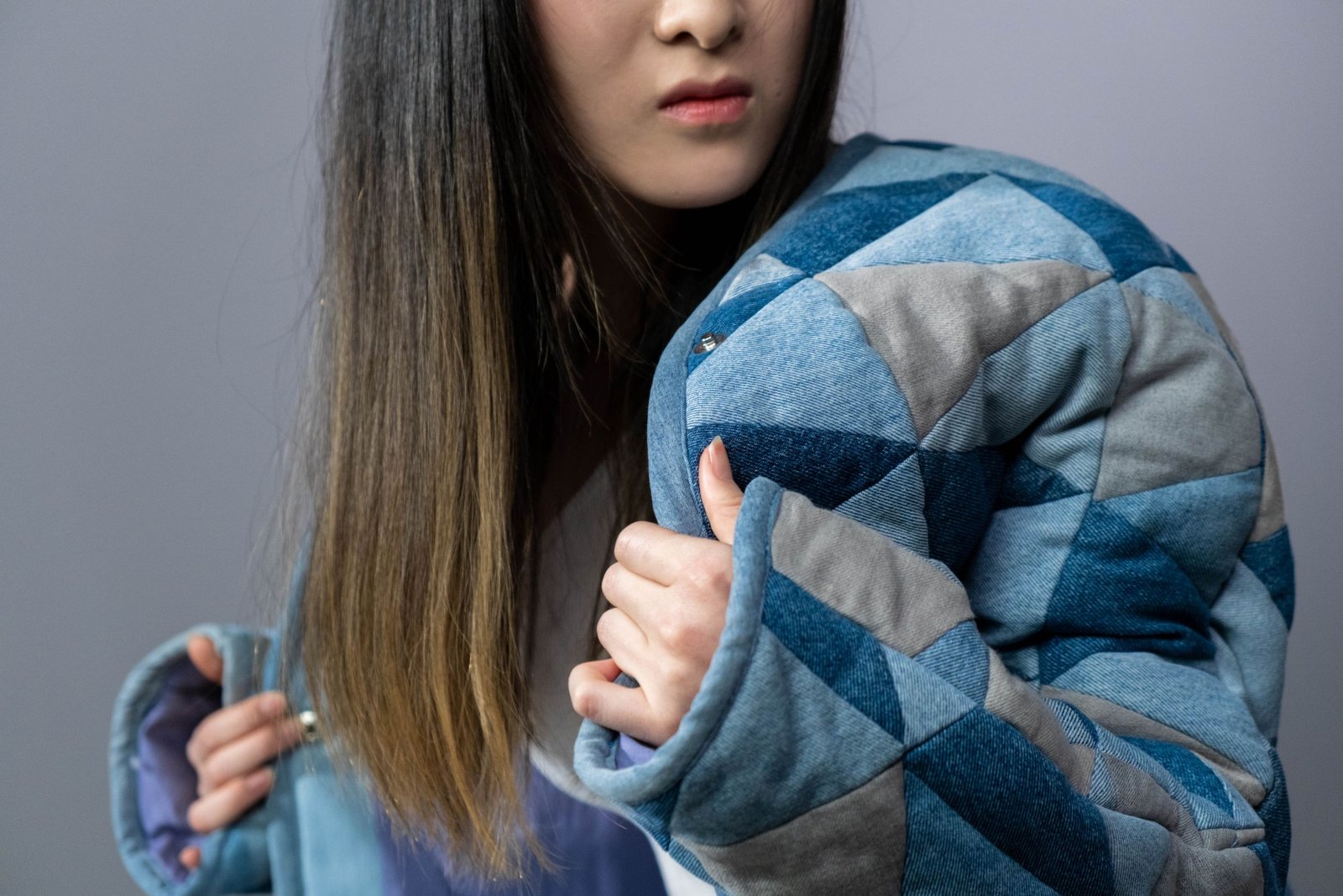 A fashionable woman poses in a denim jacket against a gray studio background.