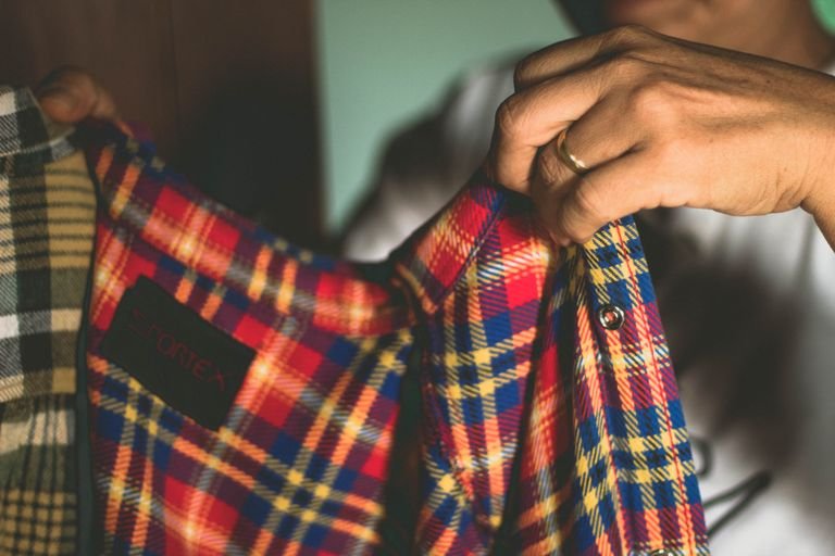 Detailed close-up of hands holding colorful plaid shirts, showcasing textile fashion and design.