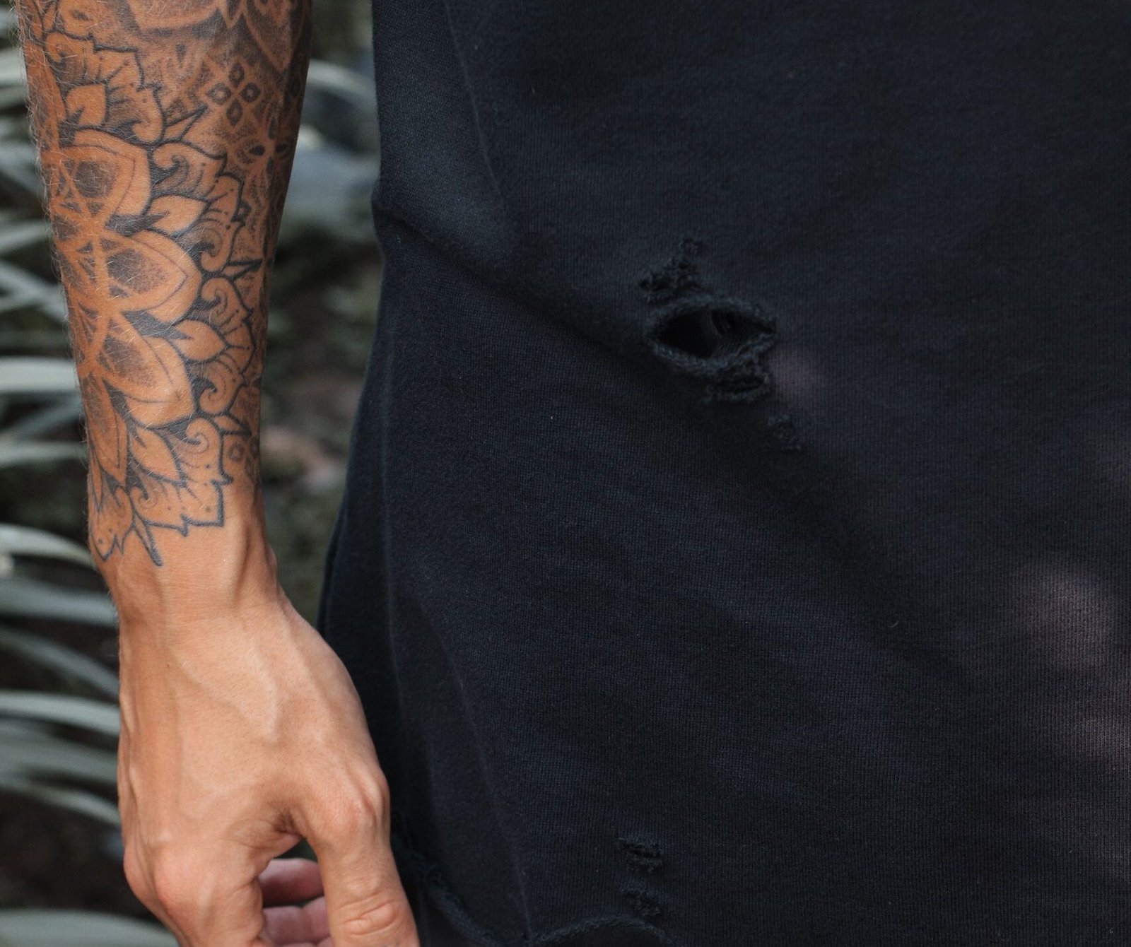Detailed view of a tattooed arm wearing casual black clothing, outdoors.