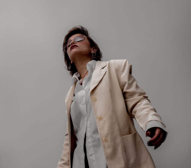 Stylish woman wearing a beige suit and sunglasses, posing against a neutral backdrop.